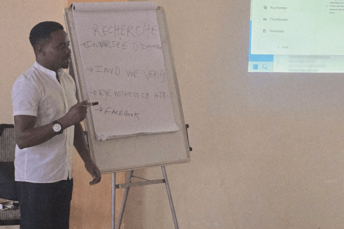 Donatien of the Integrated Refugee Organisation points to a flip-chart of verification tools while leading an OSINT session