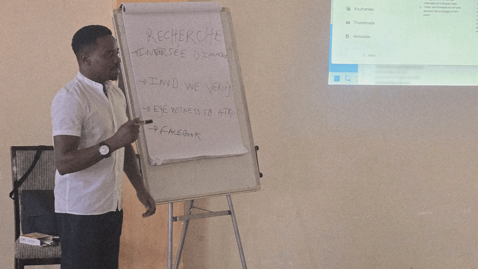 Donatien of the Integrated Refugee Organisation points to a flip-chart of verification tools while leading an OSINT session